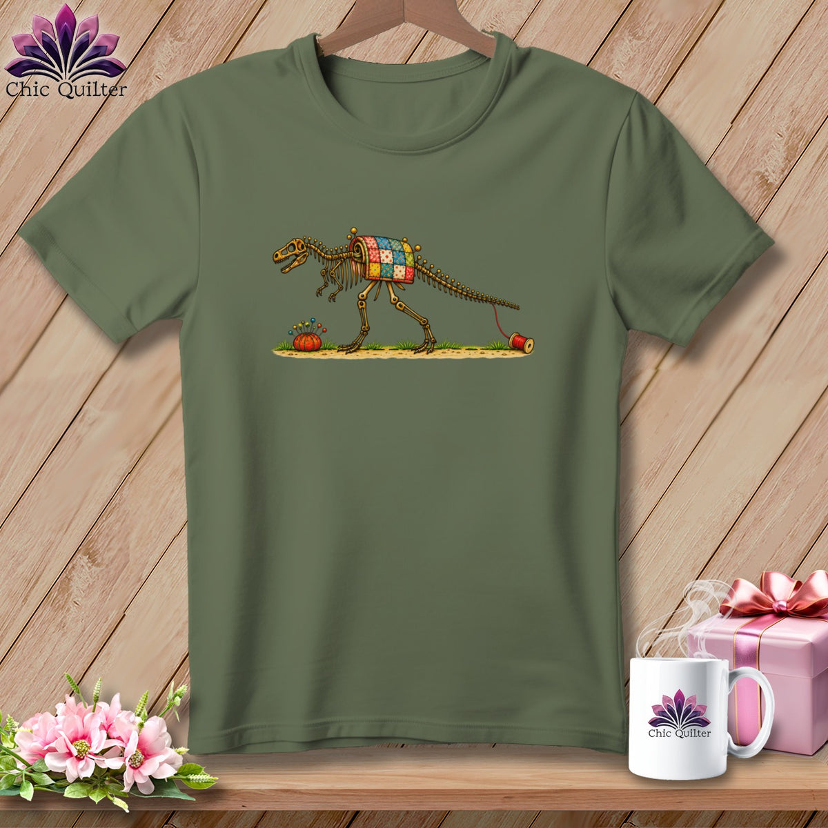 An olive green t-shirt displays an illustration of a dinosaur skeleton wearing a patchwork quilt.