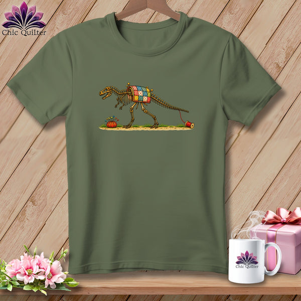 An olive green t-shirt displays an illustration of a dinosaur skeleton wearing a patchwork quilt.