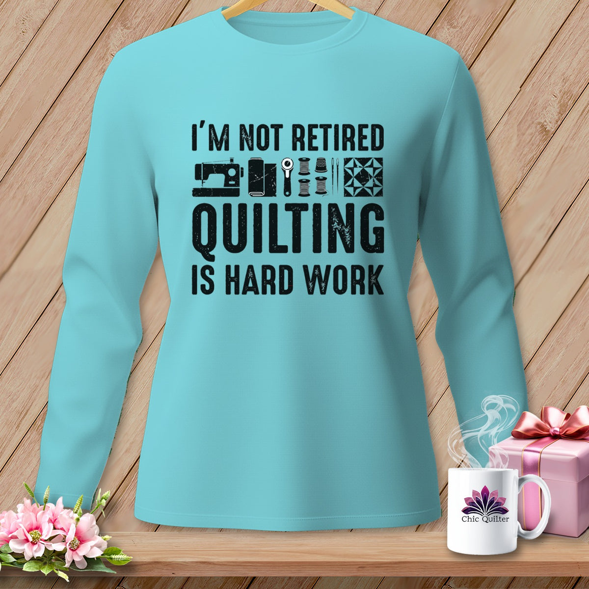 Light blue long-sleeve shirt with text "I'M NOT RETIRED QUILTING IS HARD WORK" and sewing graphics.
