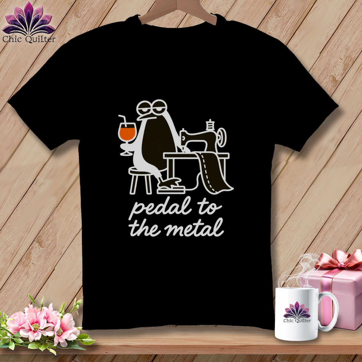 Black t-shirt with cartoon penguin at sewing machine, holding drink, text "pedal to the metal".