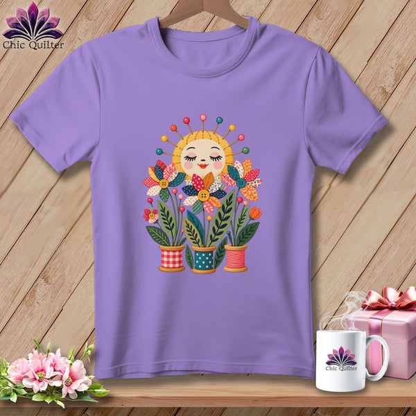A purple t-shirt featuring a graphic of a smiling sun and colorful fabric flowers in spools.