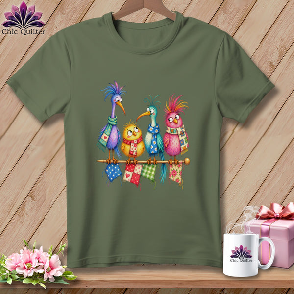 An olive green t-shirt displays a whimsical graphic of four colorful cartoon birds perched on a knitting needle.
