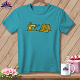 Teal short-sleeve t-shirt featuring a yellow sewing machine and quilt graphic with a small red heart.