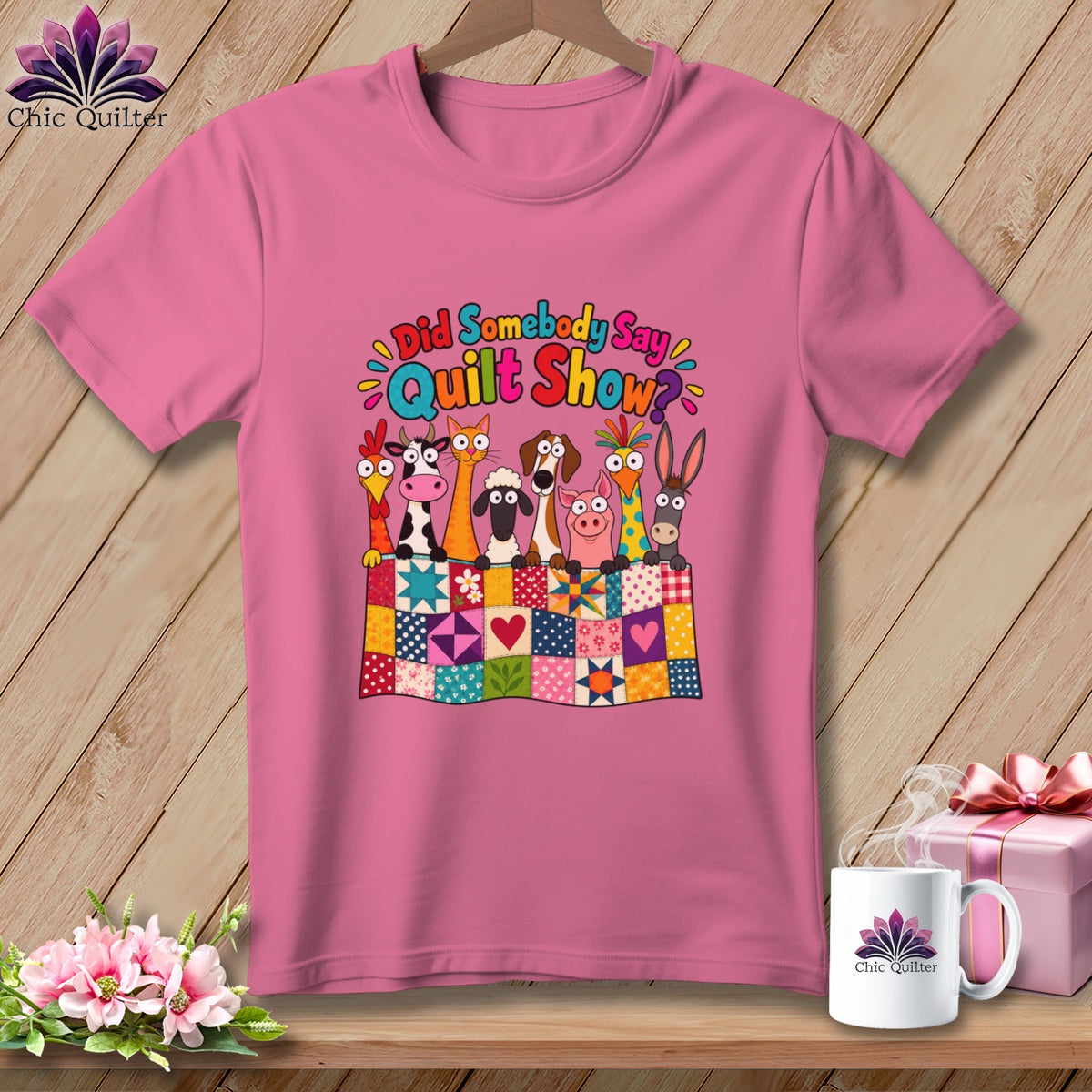 A pink t-shirt featuring cartoon farm animals behind a colorful patchwork quilt with the text Did Somebody Say Quilt Show.