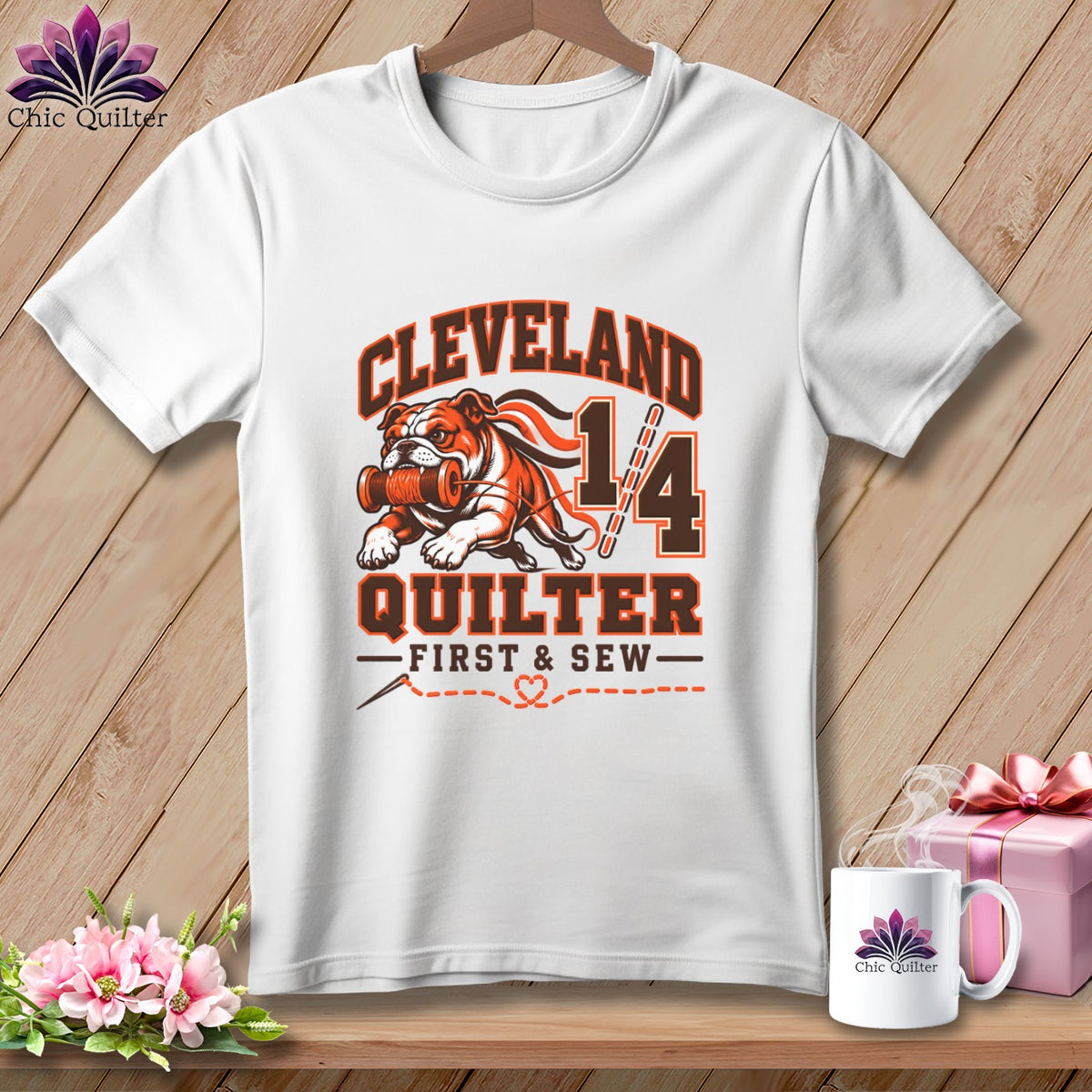 A white short-sleeve t-shirt features a graphic with a bulldog, sewing motifs, and text reading Cleveland Quilter First & Sew.