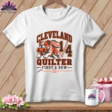 A white short-sleeve t-shirt features a graphic with a bulldog, sewing motifs, and text reading Cleveland Quilter First & Sew.