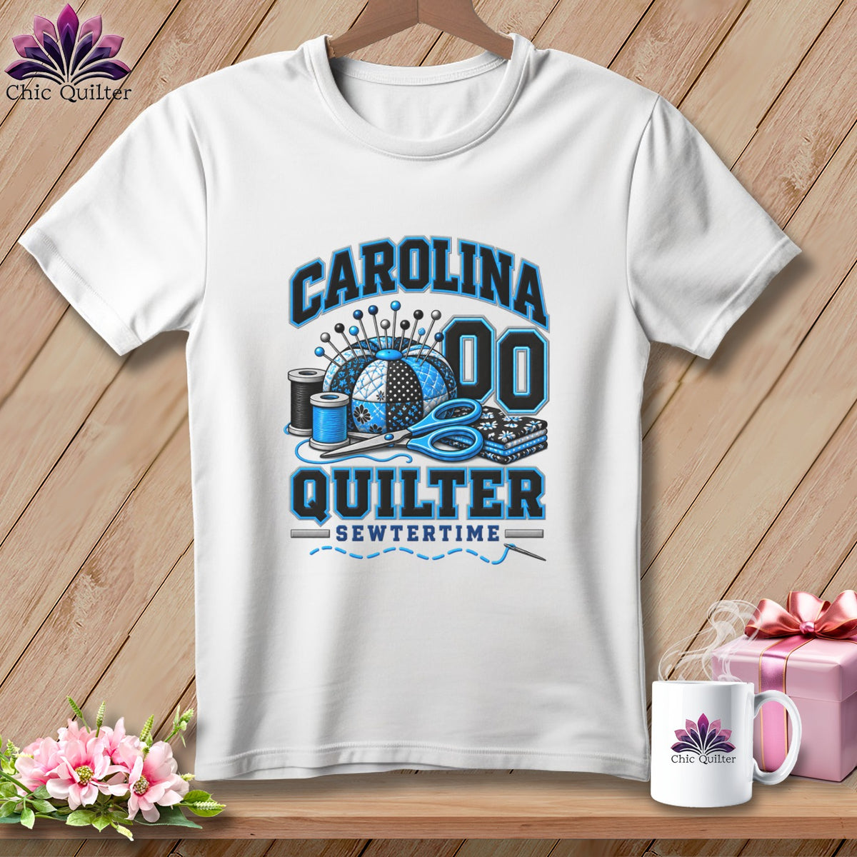 A white t-shirt hanging on a wooden background, featuring blue quilting graphic elements and text reading CAROLINA QUILTER SEWTERTIME.