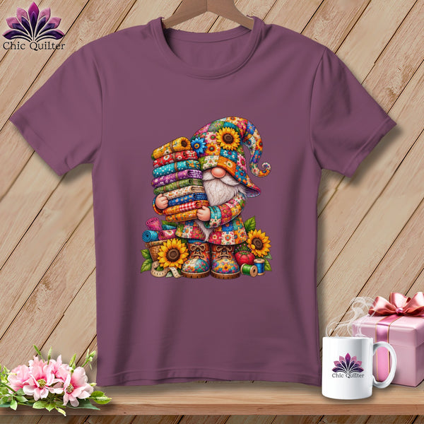 A purple t-shirt featuring a colorful gnome graphic holding stacks of fabric on a wooden background.
