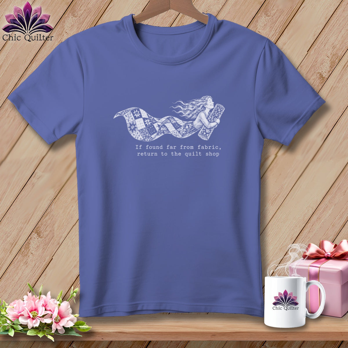 Periwinkle t-shirt with white graphic of a woman flying with a quilt and text.
