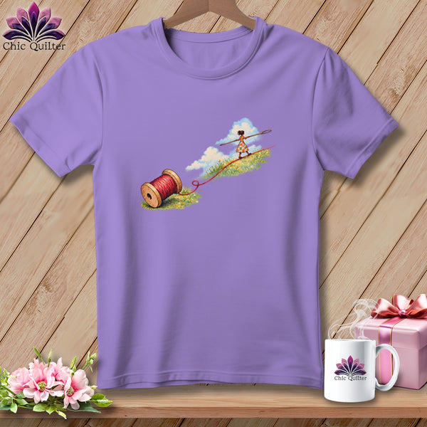 A purple t-shirt featuring a whimsical illustration of a girl tightrope walking on red thread.