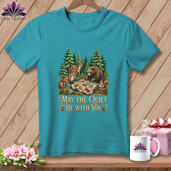 Teal short-sleeve t-shirt with a forest graphic of animals around a quilt and text reading May the Quilt Be With You.
