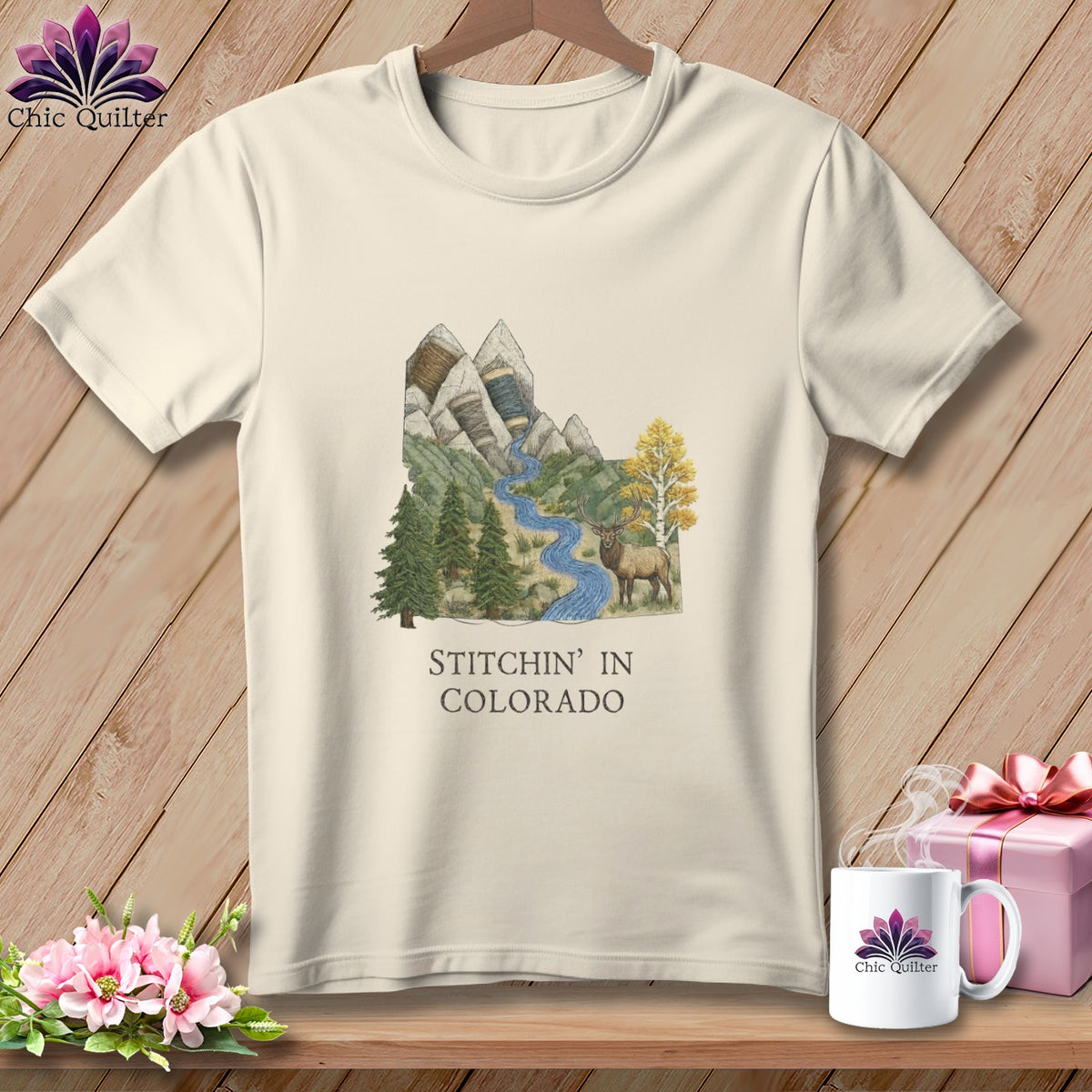 Cream t-shirt with mountain, river, elk, and text "Stitchin' in Colorado" graphic.