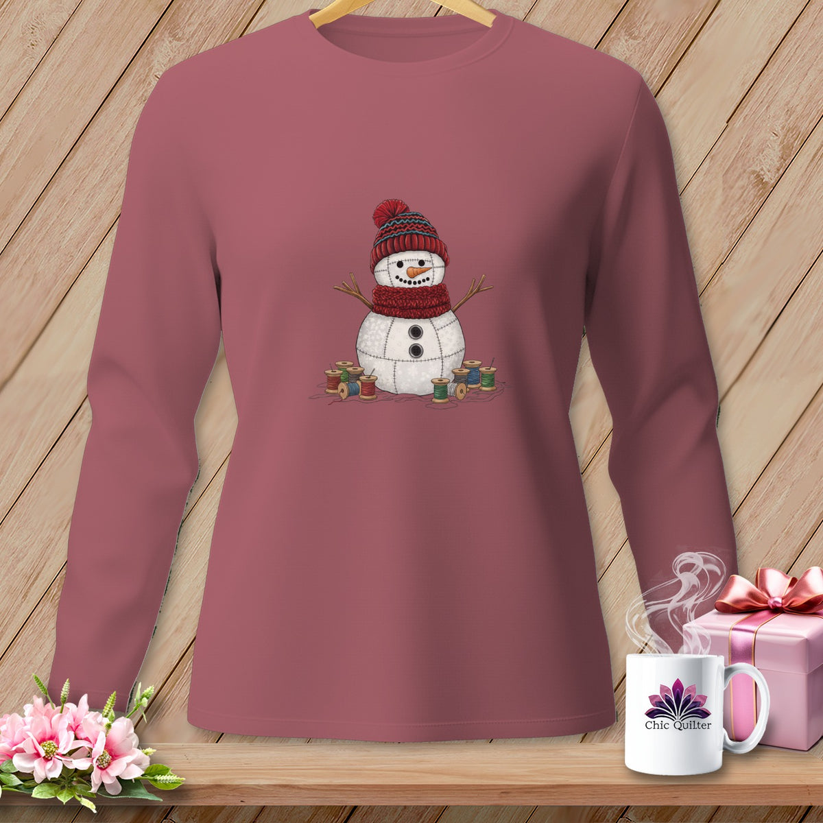 Long sleeve shirt with a stitched snowman wearing a hat and scarf, surrounded by spools of thread.