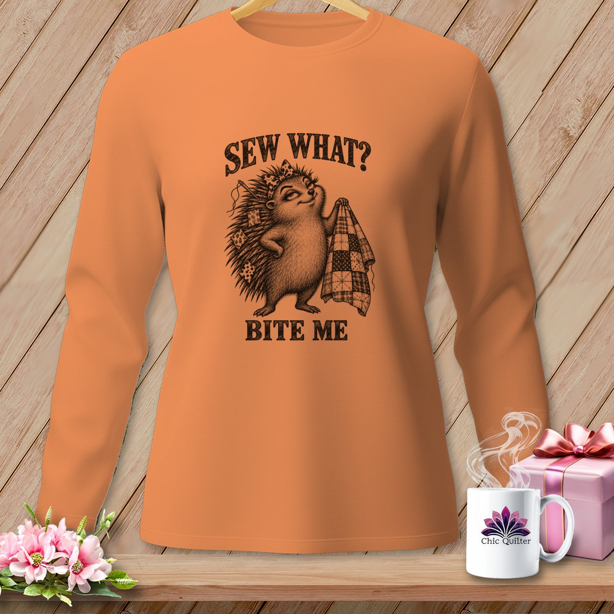 Orange long-sleeve shirt featuring a sketch of a hedgehog holding a quilt with text reading SEW WHAT? BITE ME.