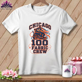 A white crewneck t-shirt features a navy and orange graphic of a bear holding a spool of thread with the text Chicago 100 Fabric Crew.
