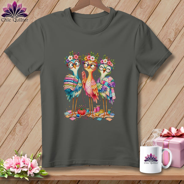 Dark gray crewneck t-shirt featuring an illustration of three colorful birds wearing glasses and flower crowns while sewing.
