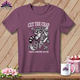 T-shirt graphic of a raccoon with rotary cutter and fabric rolls, 