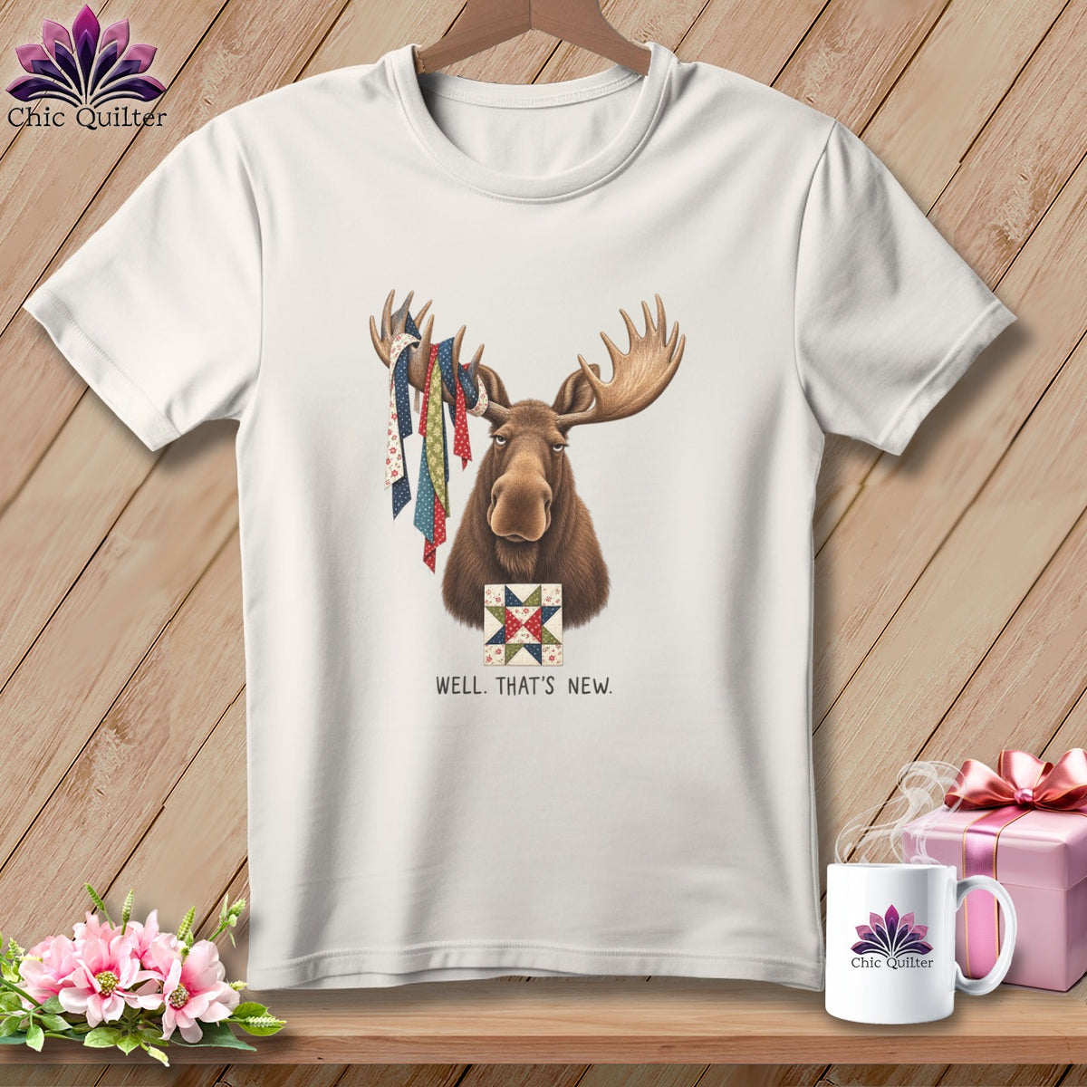 Moose wearing colorful fabric ribbons on antlers, holding quilt block, text "WELL. THAT'S NEW."