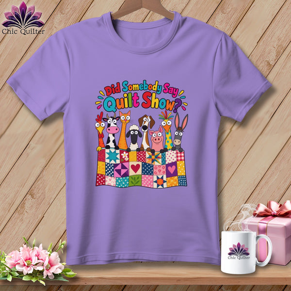 A light purple t-shirt features a colorful graphic of cartoon farm animals behind a patchwork quilt.