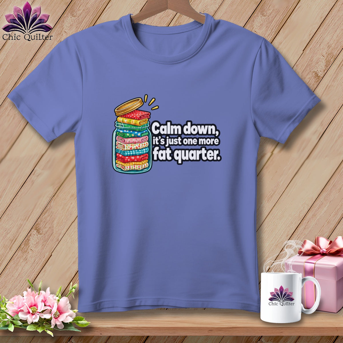 A periwinkle t-shirt features a graphic of a jar overflowing with folded fabric and text reading, Calm down, its just one more fat quarter.