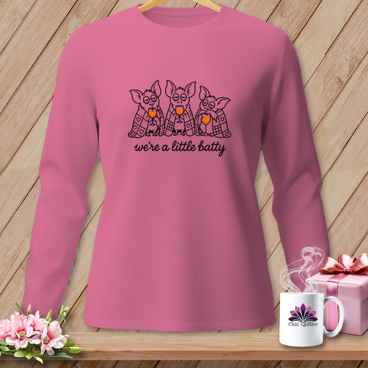Pink long-sleeve shirt with three cartoon bats holding wine glasses and the text "we're a little batty."