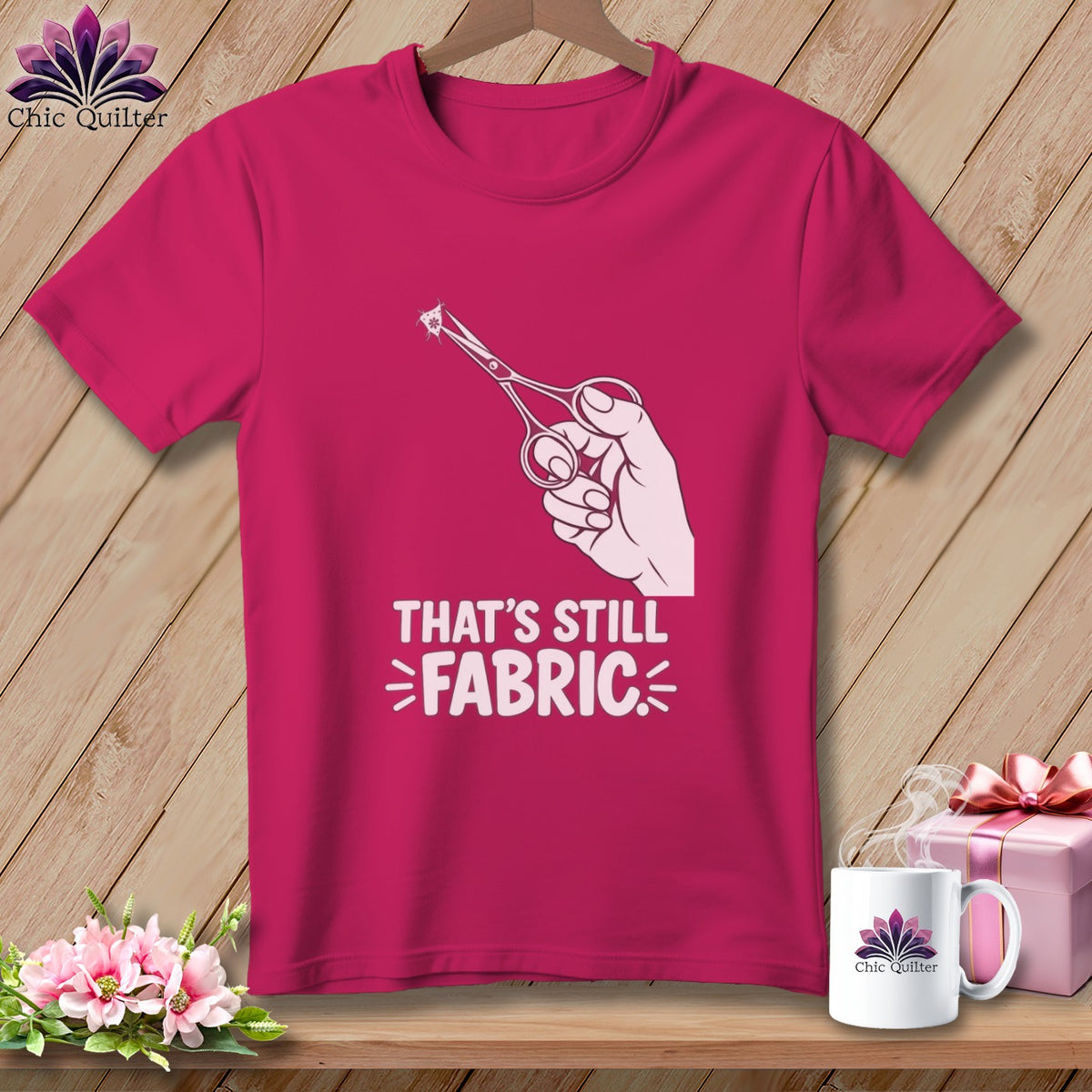 Pink t-shirt with a hand holding scissors cutting fabric, text reads "That's Still Fabric."