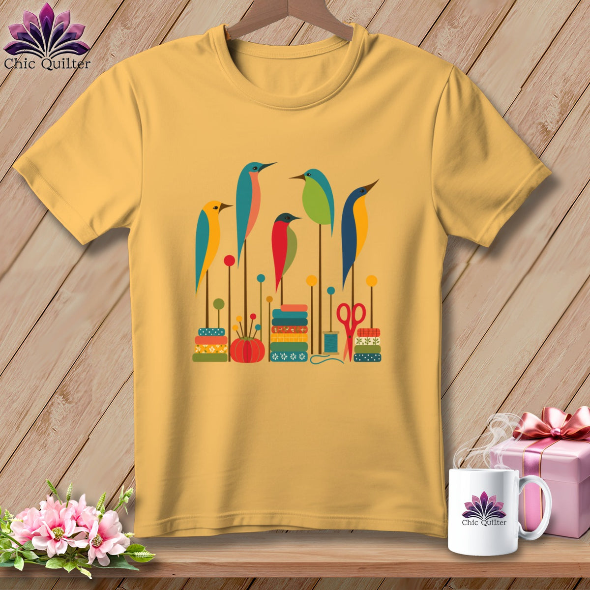 A yellow t-shirt features a graphic print of colorful stylized birds and sewing items on a wooden background.