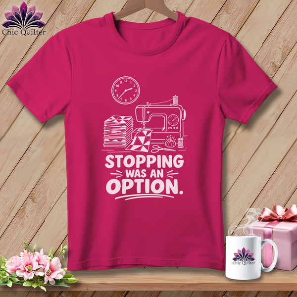 Pink t-shirt with sewing machine, fabric, clock, and "Stopping Was An Option" text.