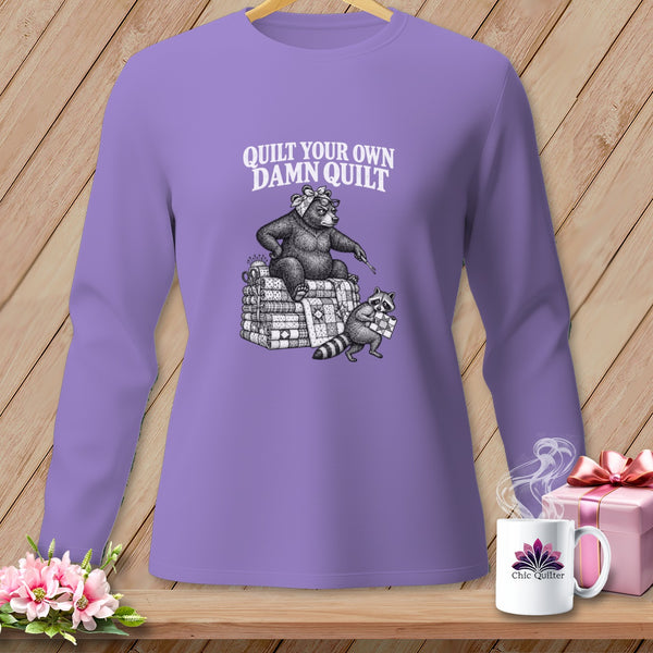Purple long-sleeve t-shirt with a graphic of a bear and raccoon on quilts and text reading Quilt Your Own Damn Quilt.