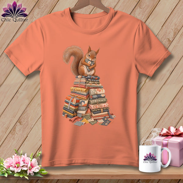 Orange t-shirt with a squirrel sitting on a stack of fabric quilts.