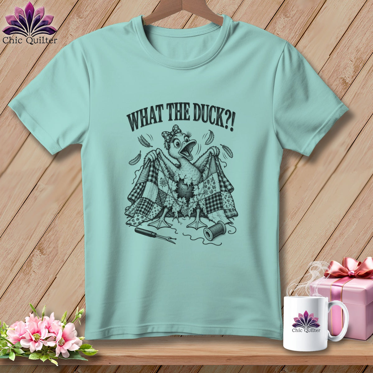 Light blue t-shirt featuring a cartoon duck holding a patchwork quilt and the text WHAT THE DUCK?!