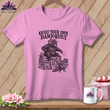 Pink t-shirt with a bear on a quilt stack and text reading QUILT YOUR OWN DAMN QUILT.