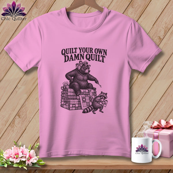 Pink t-shirt with a bear on a quilt stack and text reading QUILT YOUR OWN DAMN QUILT.