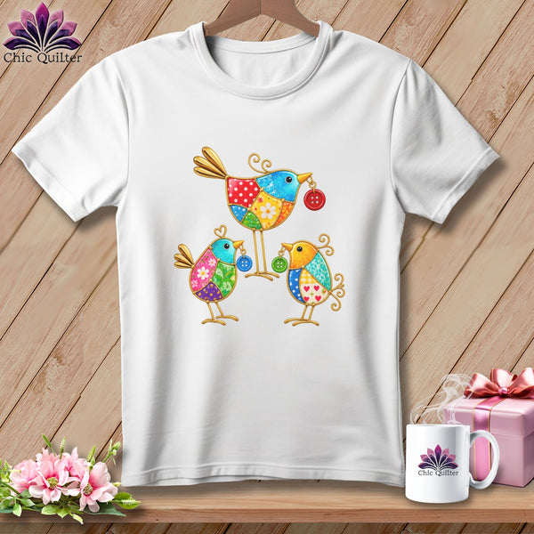 A white t-shirt featuring a colorful patchwork design of three stylized birds holding buttons.
