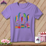 Lavender t-shirt featuring a colorful graphic of five stylized birds perched on sewing supplies against a wooden background.