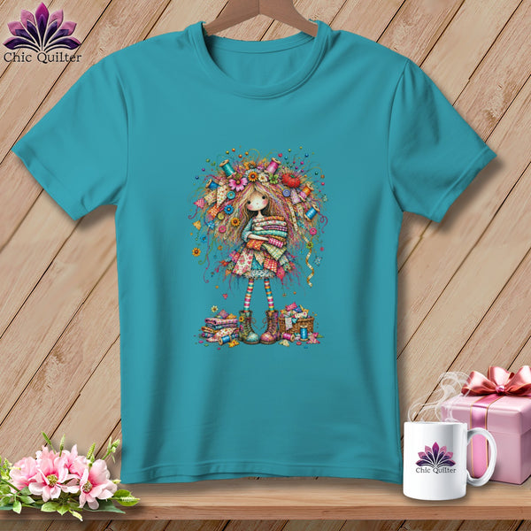 A turquoise t-shirt on a wooden hanger features an illustration of a girl surrounded by sewing notions.