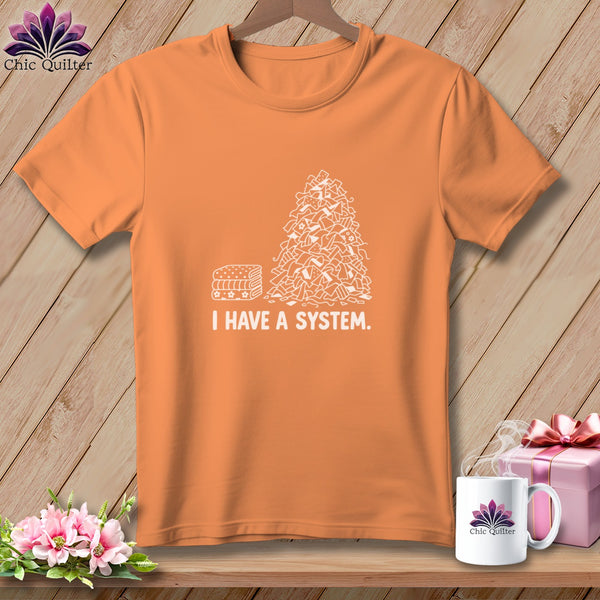 Orange t-shirt with a pile of fabric scraps and stacked fabric next to "I HAVE A SYSTEM."