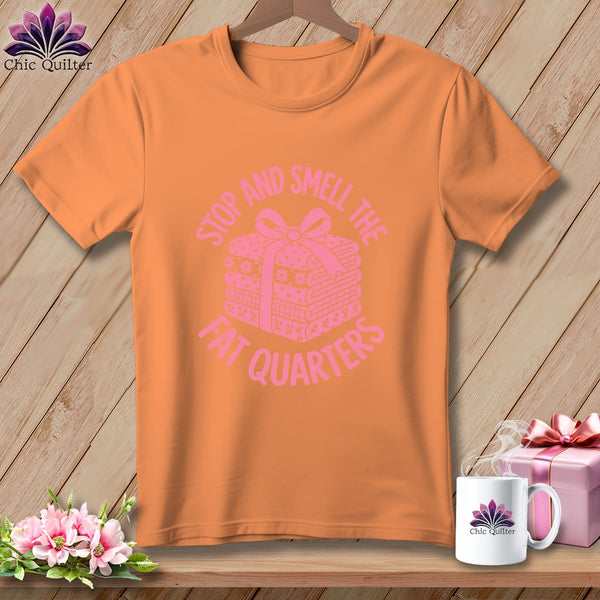 Orange short-sleeve t-shirt with pink text reading "STOP AND SMELL THE FAT QUARTERS" and a stack of fabric quarters.