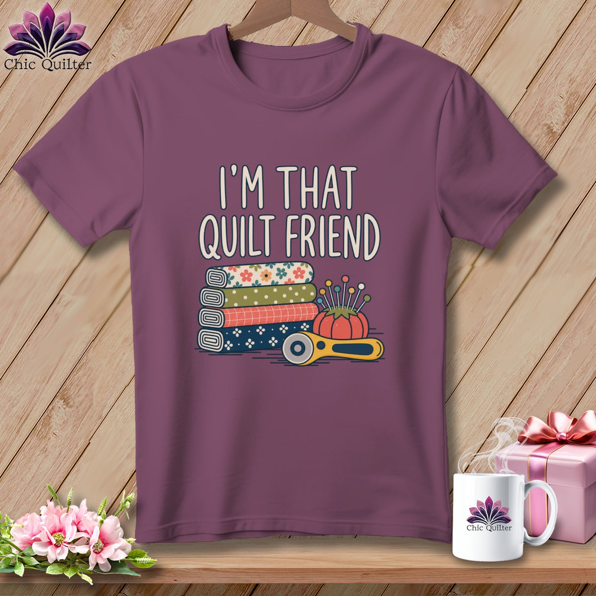 A purple crewneck t-shirt featuring the text I'M THAT QUILT FRIEND above stacked fabric rolls, a pincushion, and a rotary cutter.
