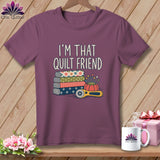 A purple crewneck t-shirt featuring the text I'M THAT QUILT FRIEND above stacked fabric rolls, a pincushion, and a rotary cutter.