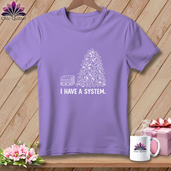 Purple t-shirt with white line drawing of fabric scraps and stacked fabric.