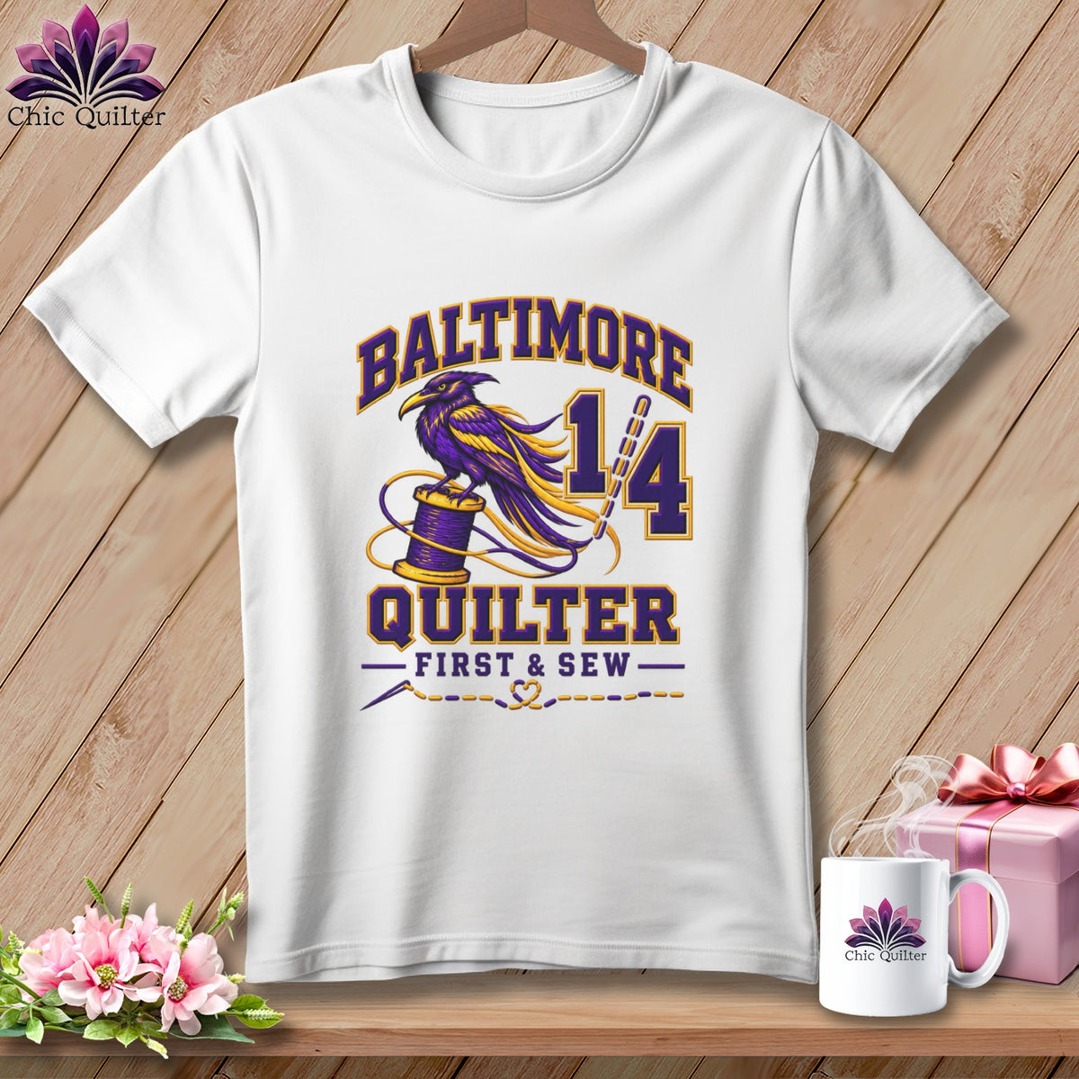 A white t-shirt hanging on a wooden background features a purple and yellow raven graphic with Baltimore Quilter First & Sew text.