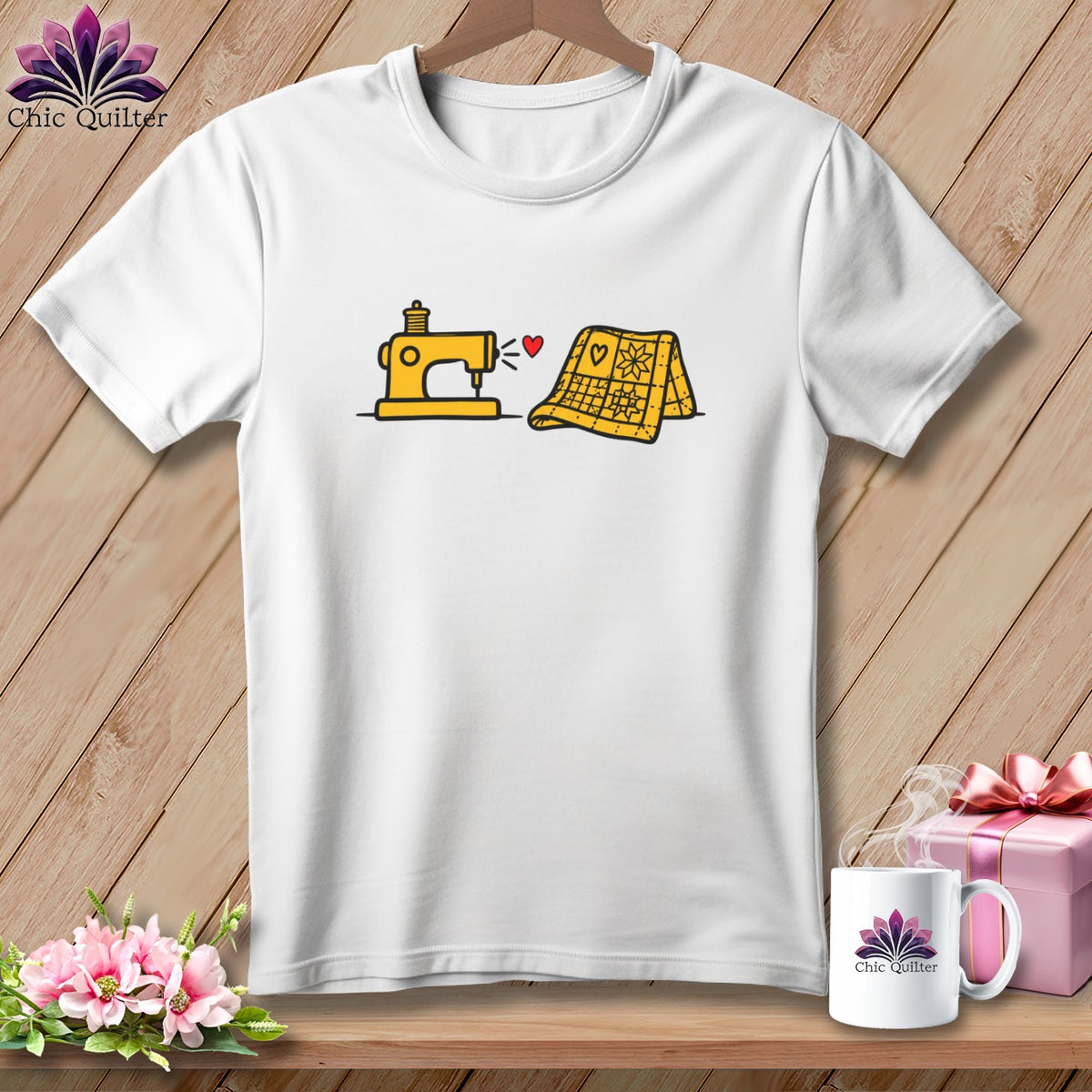 A white short-sleeved t-shirt featuring a graphic of a yellow sewing machine sewing a yellow quilt, with a small red heart above the machine.