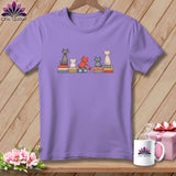 A purple t-shirt featuring an illustration of five cats sitting on patterned cushions.