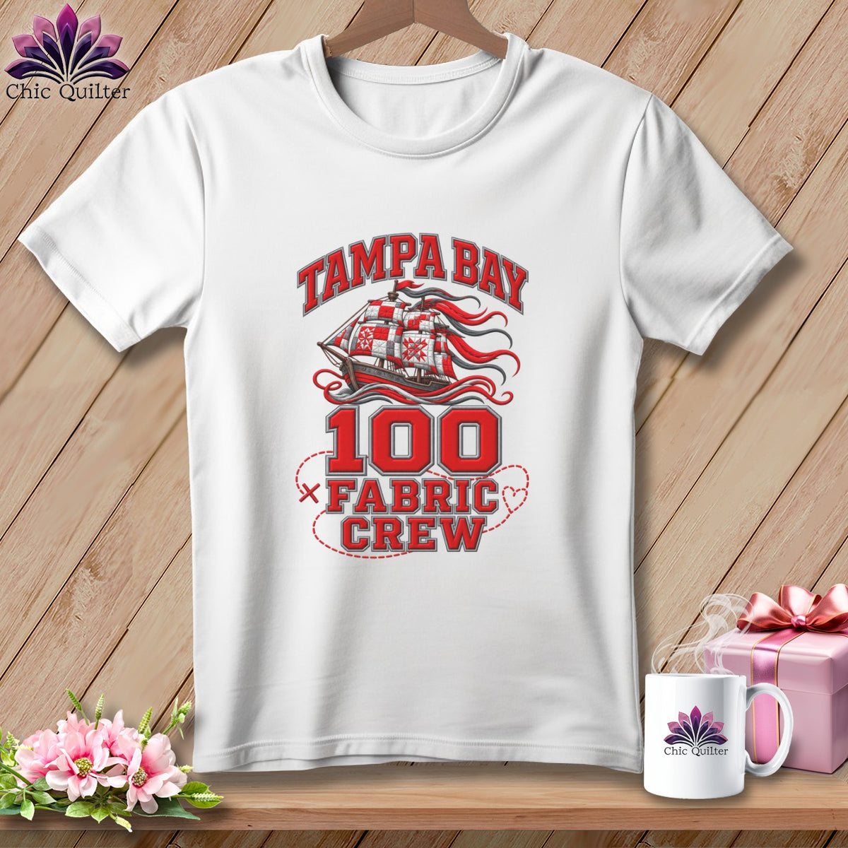 A white short-sleeve t-shirt features a red graphic with a pirate ship, the number 100, and text reading Tampa Bay Fabric Crew.