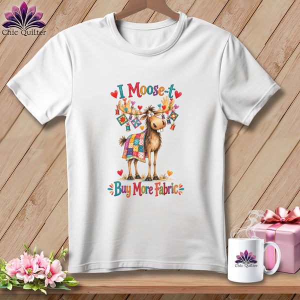 White t-shirt with a cartoon moose draped in a quilt, accompanied by the text "I Moose-t Buy More Fabric."