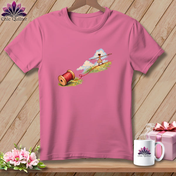 A pink short-sleeved t-shirt featuring a graphic of a girl tightrope walking on red thread.