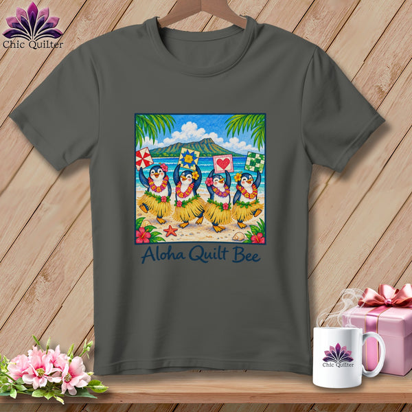 Dark gray t-shirt featuring a graphic of four penguins hula dancing on a beach under the text "Aloha Quilt Bee".