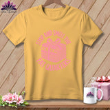 A yellow t-shirt features a pink graphic of a folded stack of fabric tied with a ribbon, surrounded by the text 