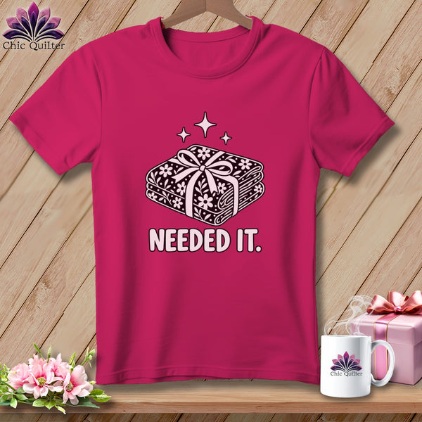 Pink t-shirt with a graphic of stacked fabric bundles tied with a bow, reading "NEEDED IT."